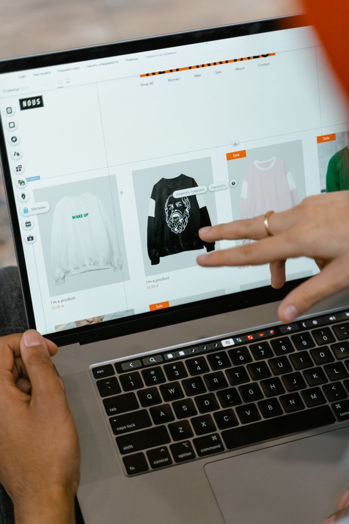 Vue rapprochée de mains utilisant un site d'achat sur l'écran d'un ordinateur portable, en intérieur.